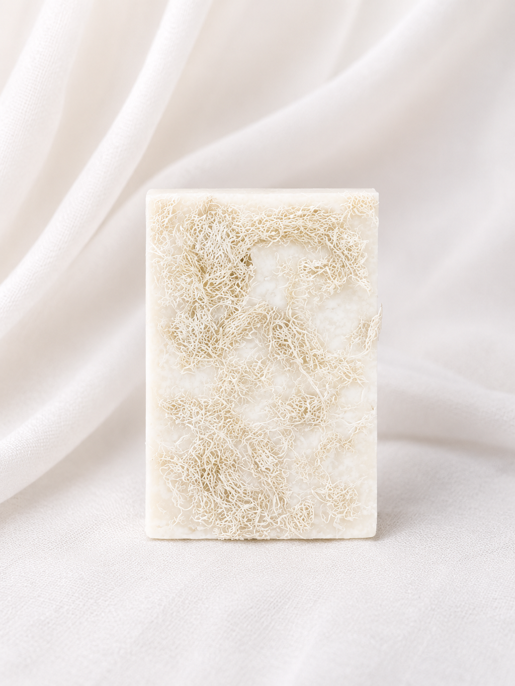 Natural loofah soap bar with embedded loofah fibers, handmade for gentle exfoliation and daily cleansing, displayed on a soft neutral fabric background.