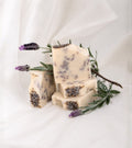 Natural handmade lavender soap with real lavender buds, artisan soap bars styled with fresh lavender stems on an elegant neutral fabric backdrop.