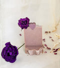 Handcrafted rose soap with a soft blush pink color, decorated with a dried rose bloom and heart-shaped soap embellishment, displayed in an elegant botanical setting.