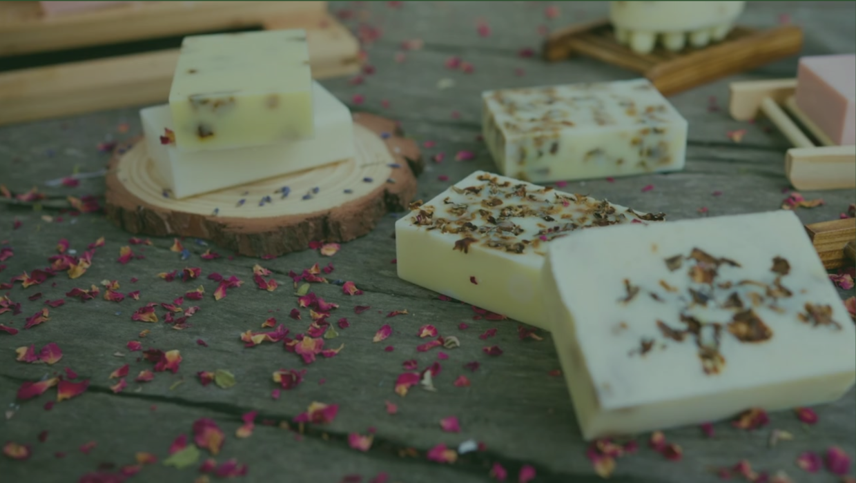 Handmade soap bars with dried botanical toppings arranged on a rustic wooden surface.
