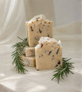 Natural handmade rosemary soap with real rosemary botanicals, stacked artisan soap bars styled with fresh rosemary sprigs on an elegant neutral fabric background.