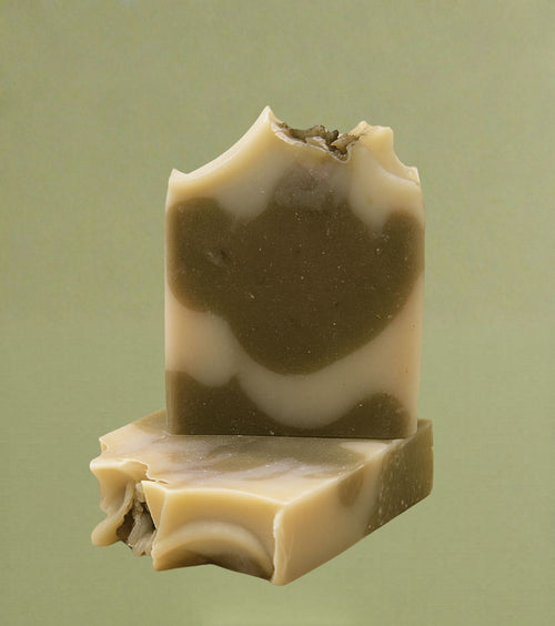 Two stacked bars of handmade clove bud soap with beige and brown swirls, showing a smooth finish and slightly rough, artisanal edges on a neutral background.